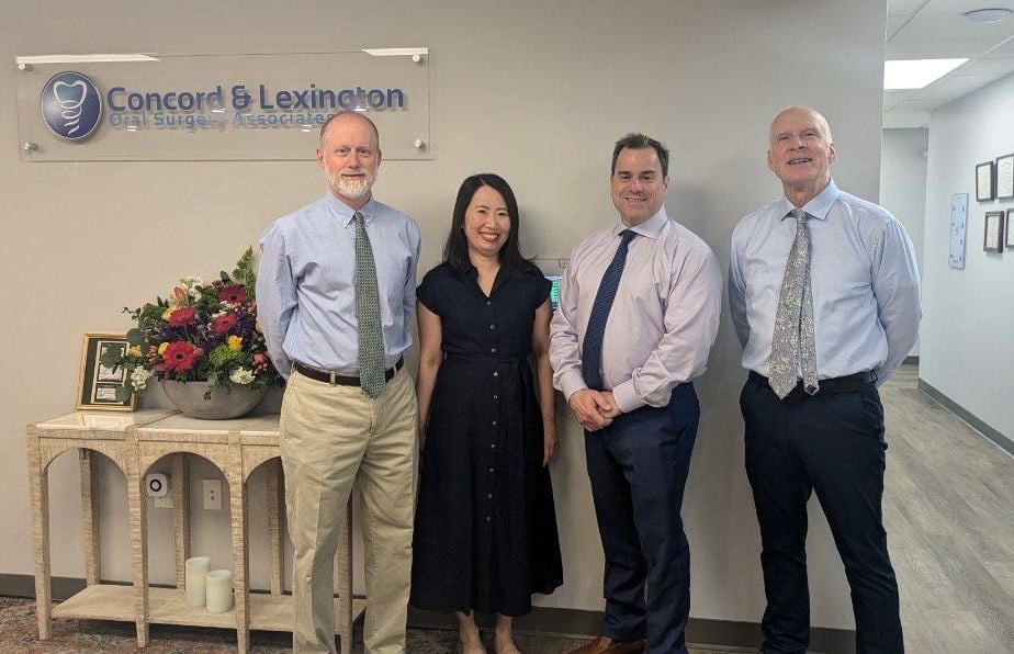 Group photo of the 4 Concord & Lexington Oral Surgeons standing in their lobby in front of their practice sign